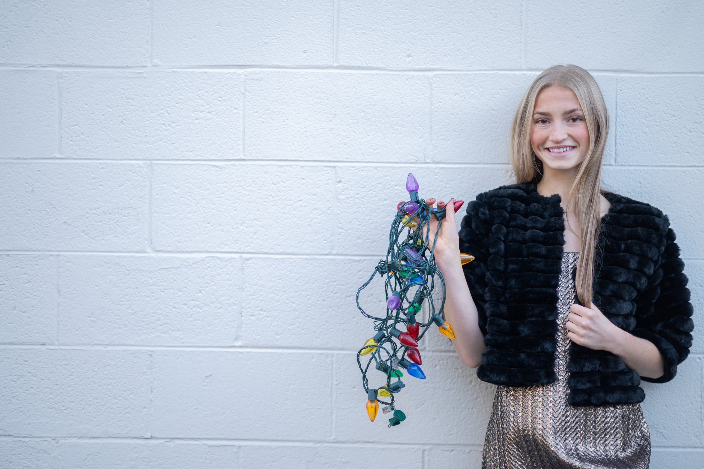Woman holding Christmas lights against a white brick wall