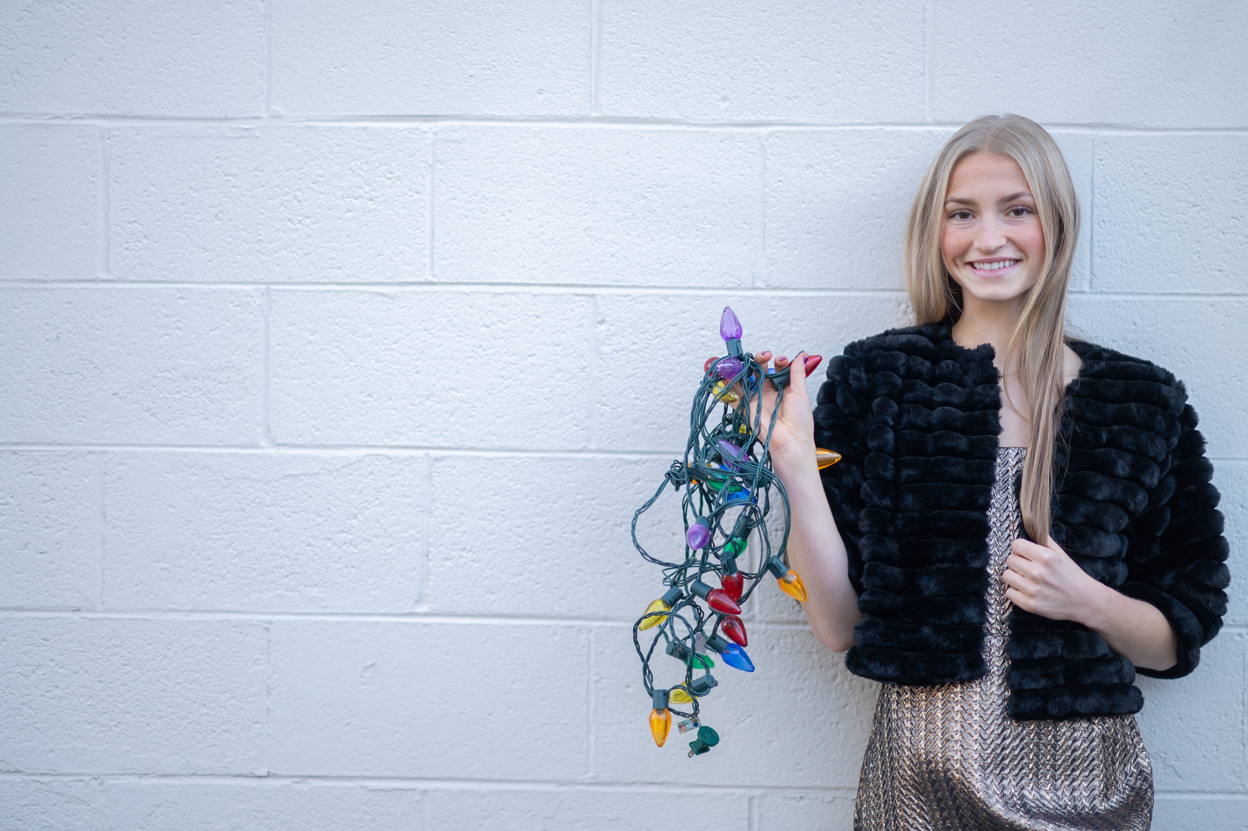 Woman holding Christmas lights against a white brick wall